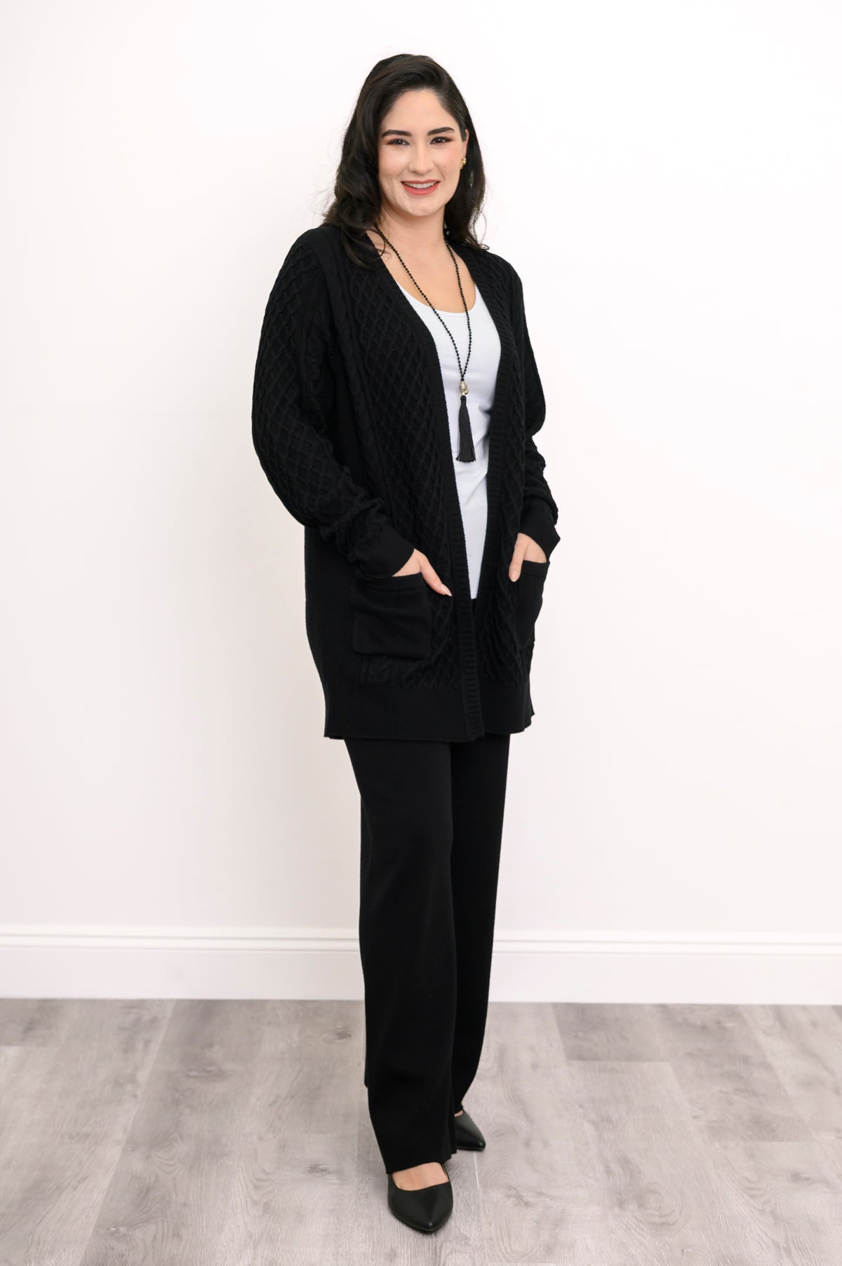 Full length shot of a woman in a longline black cotton viscose knit cardigan with front patch pockets.