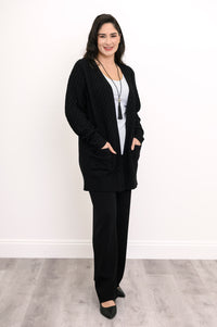 Full length shot of a woman in a longline black cotton viscose knit cardigan with front patch pockets.