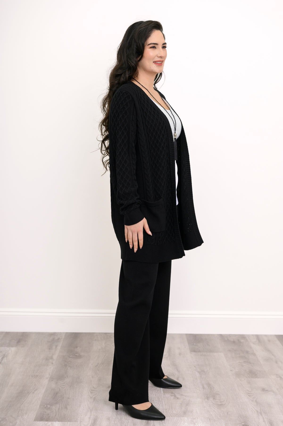 Side profile shot of a woman modeling a black long sleeve cable knit sweater for fall layering.