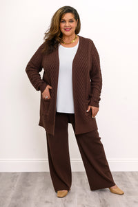 Front view of a woman with hands in pockets wearing a comfortable extended length chocolate brown knit cardigan.