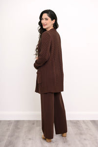 Back view of a woman wearing a hip length chocolate brown cable knit cardigan showing clean shoulder tailoring.