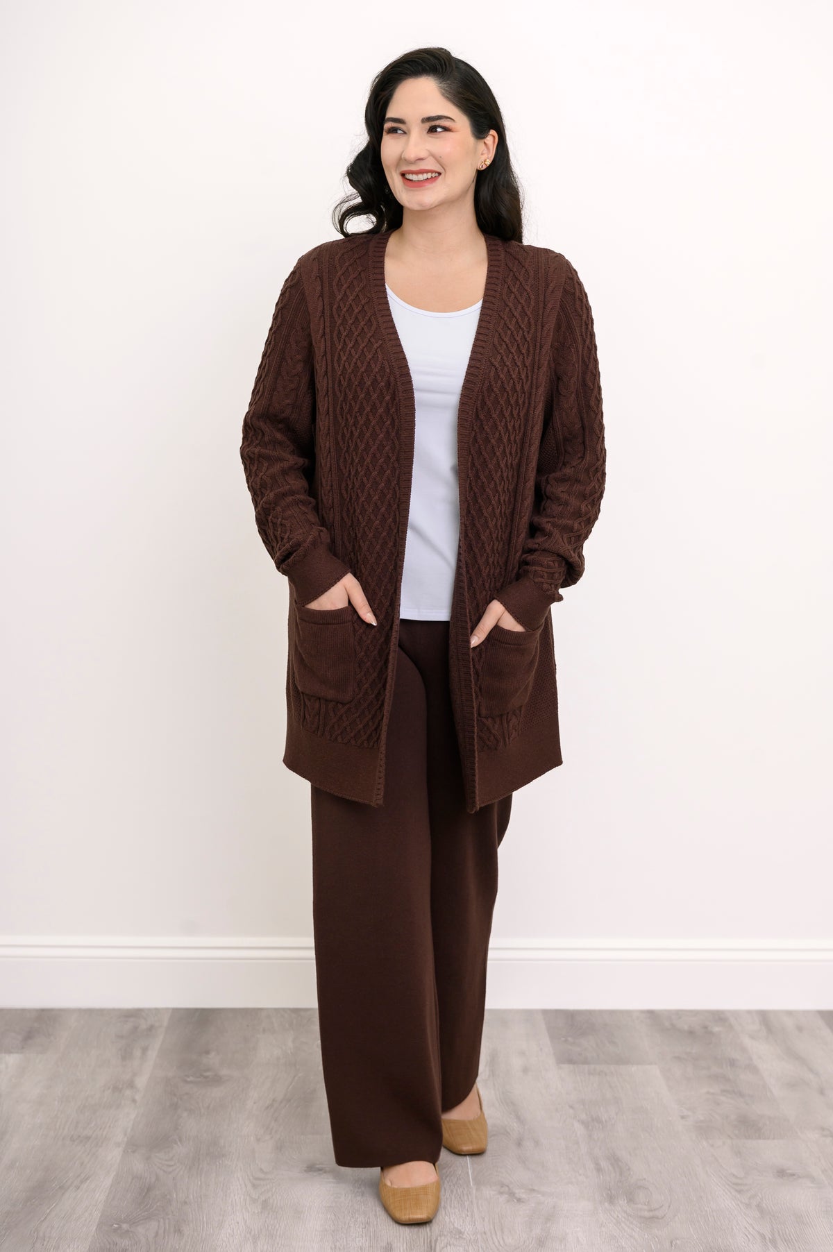 Three quarter view of a woman wearing a relaxed chocolate brown cable knit cardigan sweater for fall layering.