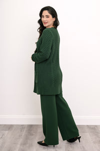 Back view of a woman wearing a hip length forest green cable knit cardigan sweater in studio.