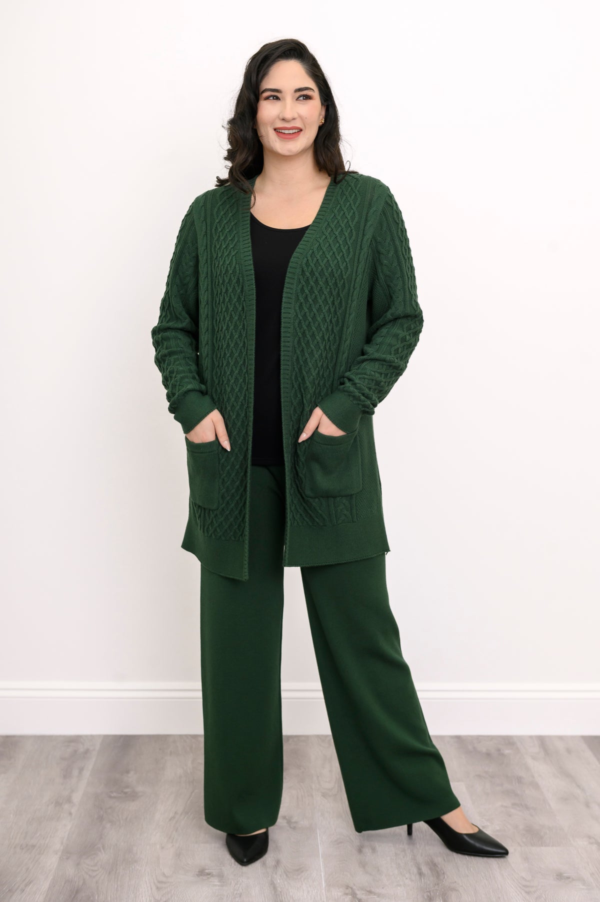 Women's forest green cable knit layering cardigan sweater with front pockets on white backdrop.