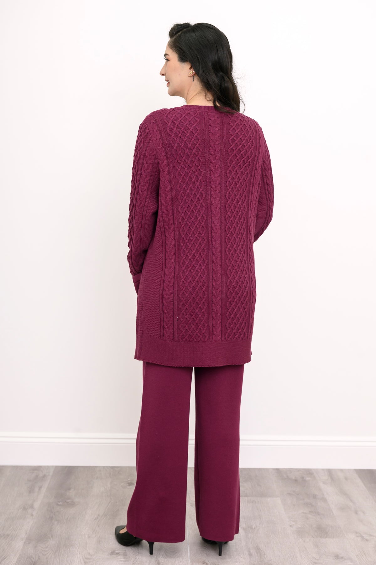 Back view of a woman wearing a hip length raspberry pink cable knit cardigan showing clean shoulder tailoring.