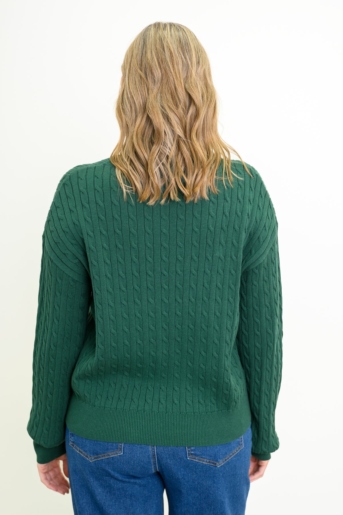 Back view of a women's long-sleeve dark green knit top, styled with blue jeans against a white backdrop.