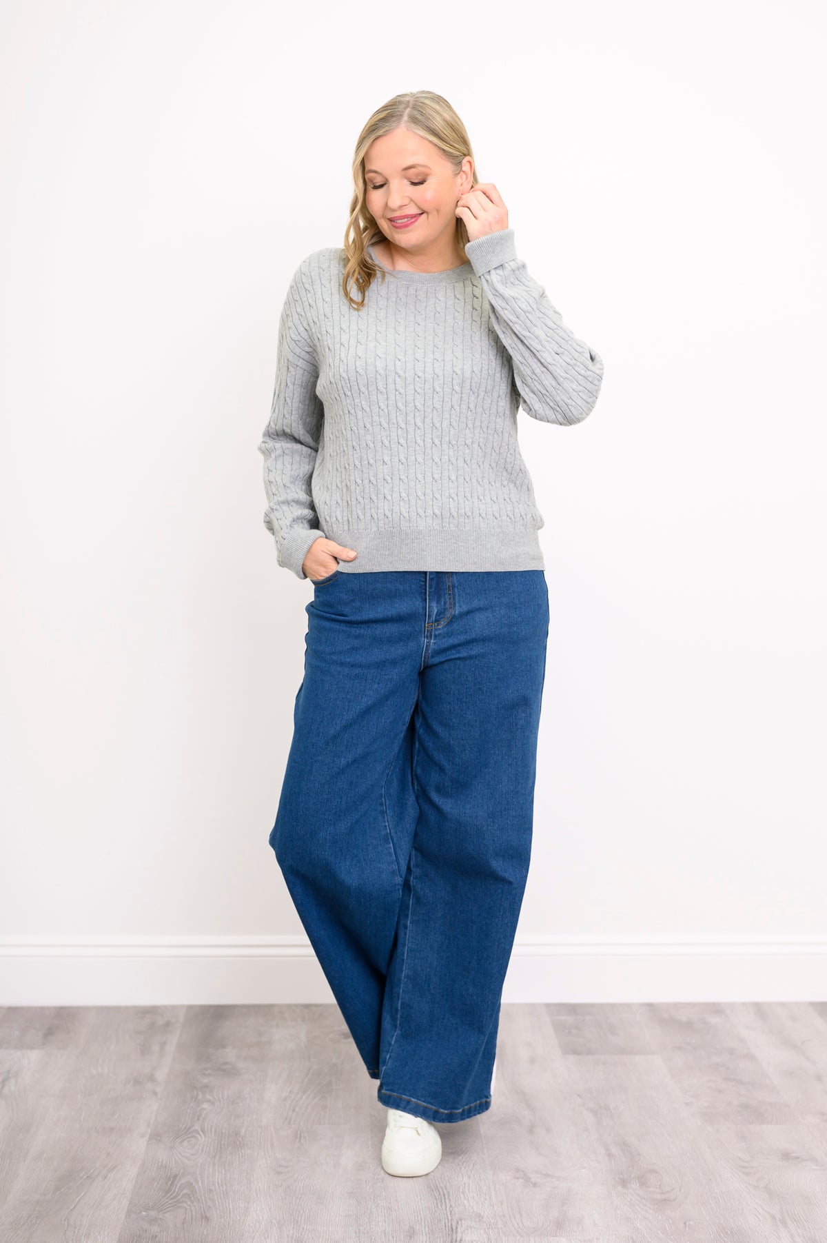 Angled view of a silver-toned long-sleeve textured sweater on a model, standing against a plain white wall.