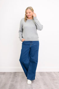 Angled view of a silver-toned long-sleeve textured sweater on a model, standing against a plain white wall.