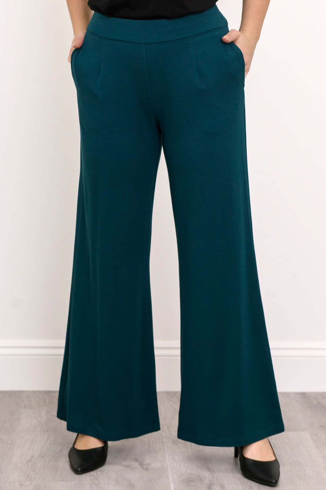 Front view of a woman wearing teal wide-leg bamboo French terry pants featuring front darts and side pockets