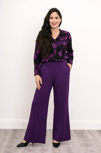 Full-length front view of a smiling woman wearing royale purple wide-leg pants paired with a patterned floral blouse.