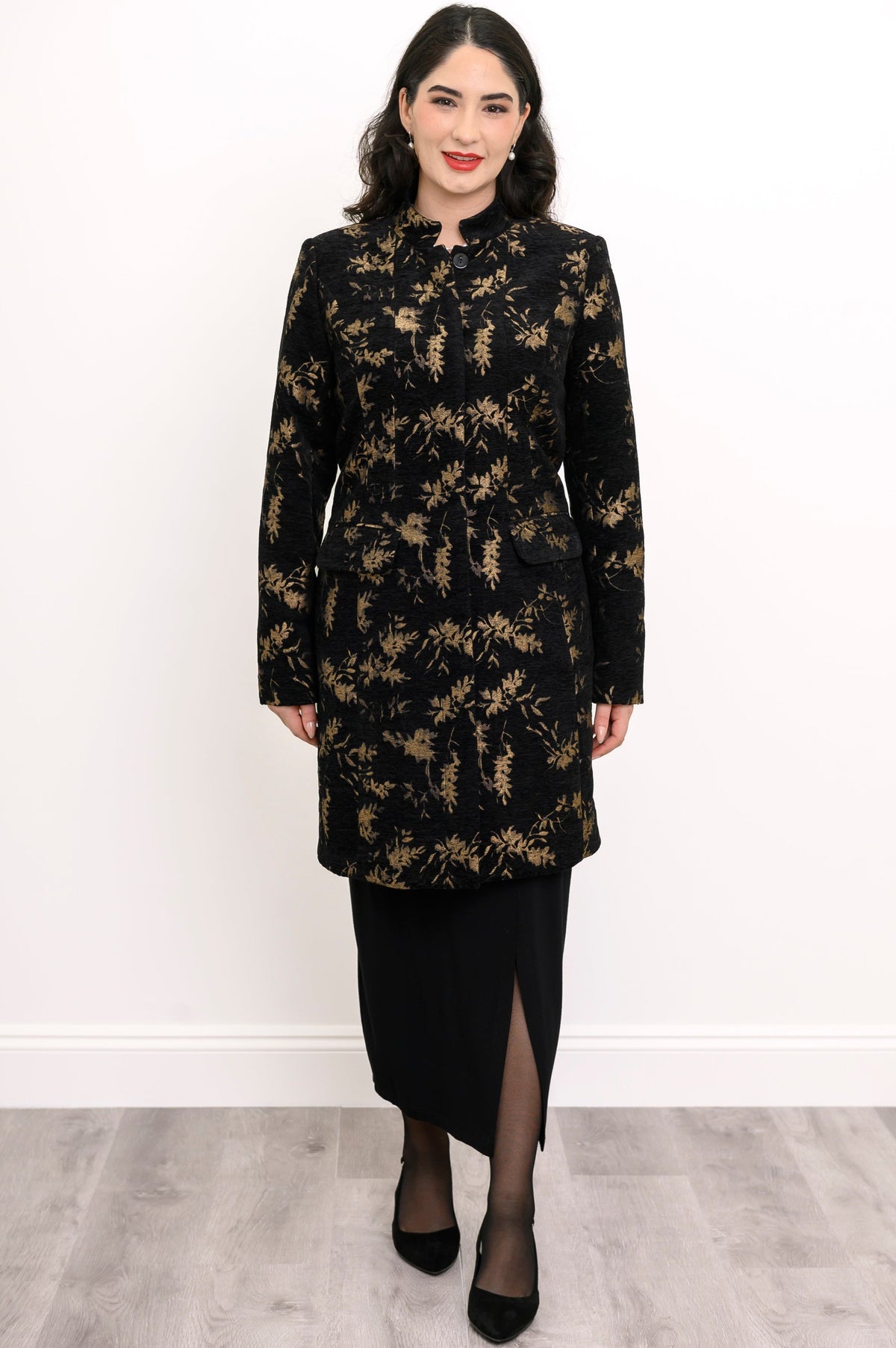Woman wearing black and gold leaf patterned coat with pockets and a black skirt on a white background, front view