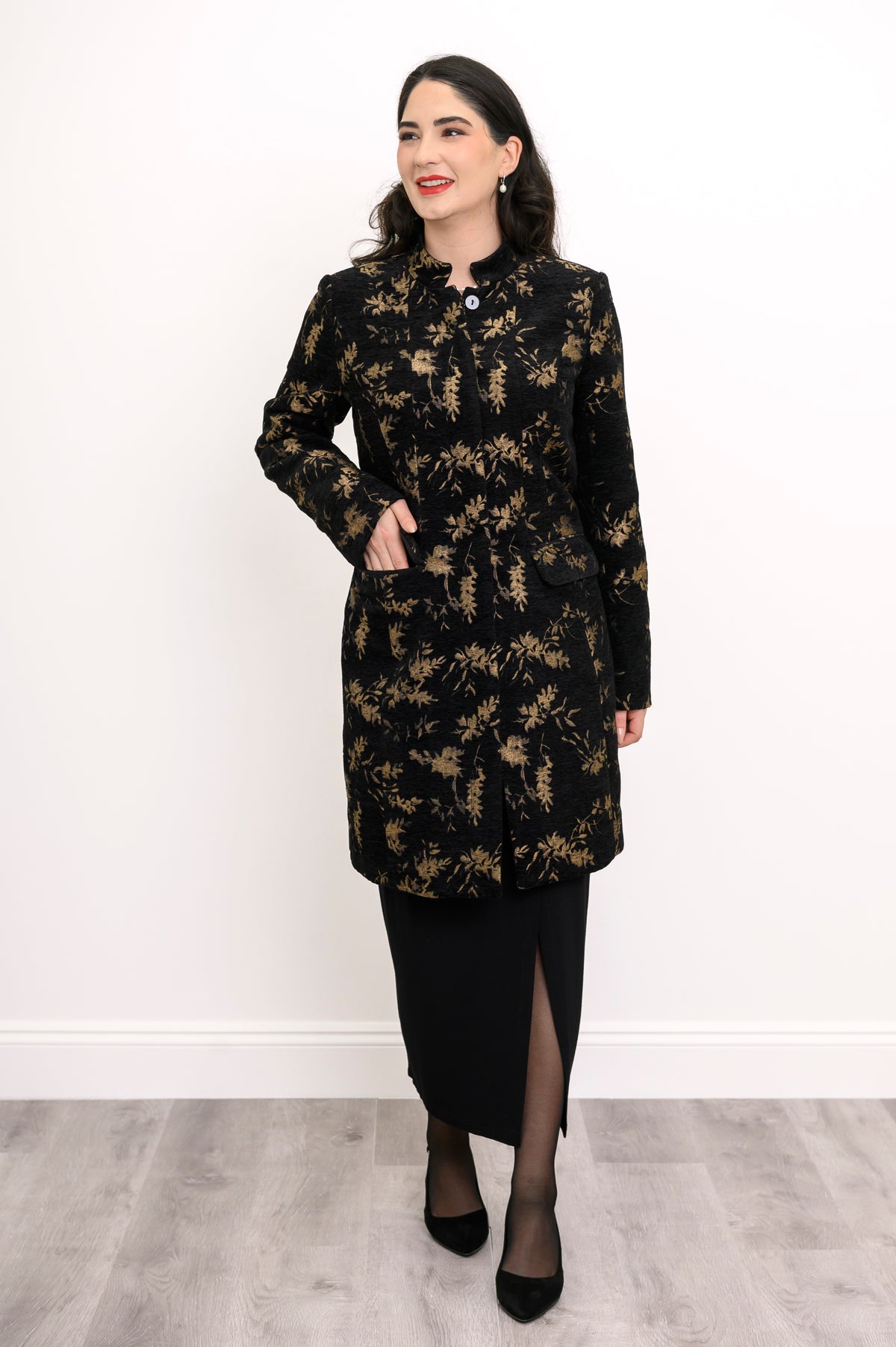 Woman wearing black and gold collared coat with pockets and a black skirt on a white background, front view