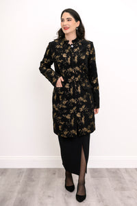 Woman wearing black and gold collared coat with pockets and a black skirt on a white background, front view