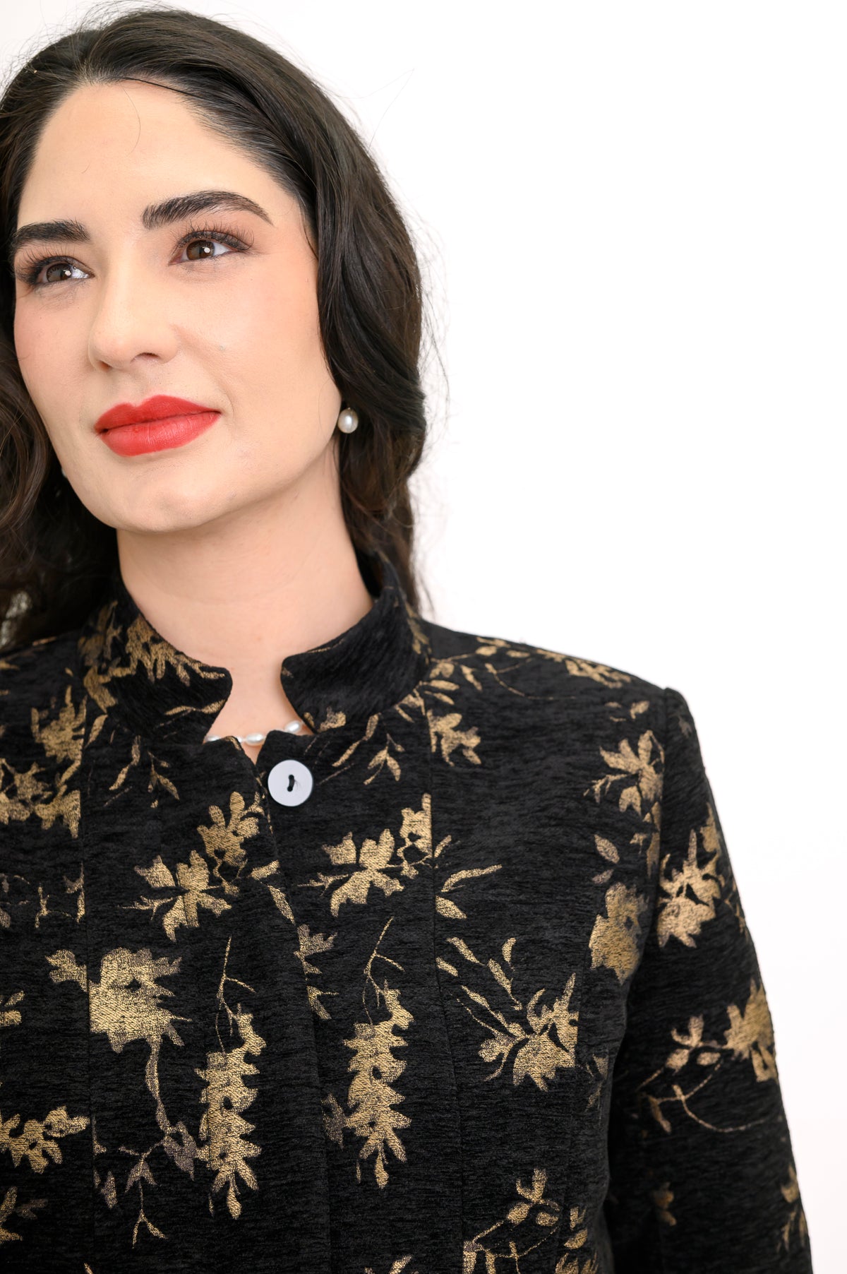 Close up view of black coat with gold leaf print, mandarin collar, and button front closure