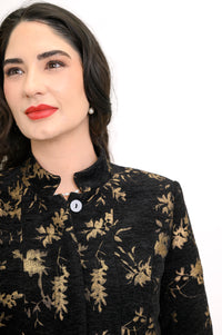Close up view of black coat with gold leaf print, mandarin collar, and button front closure