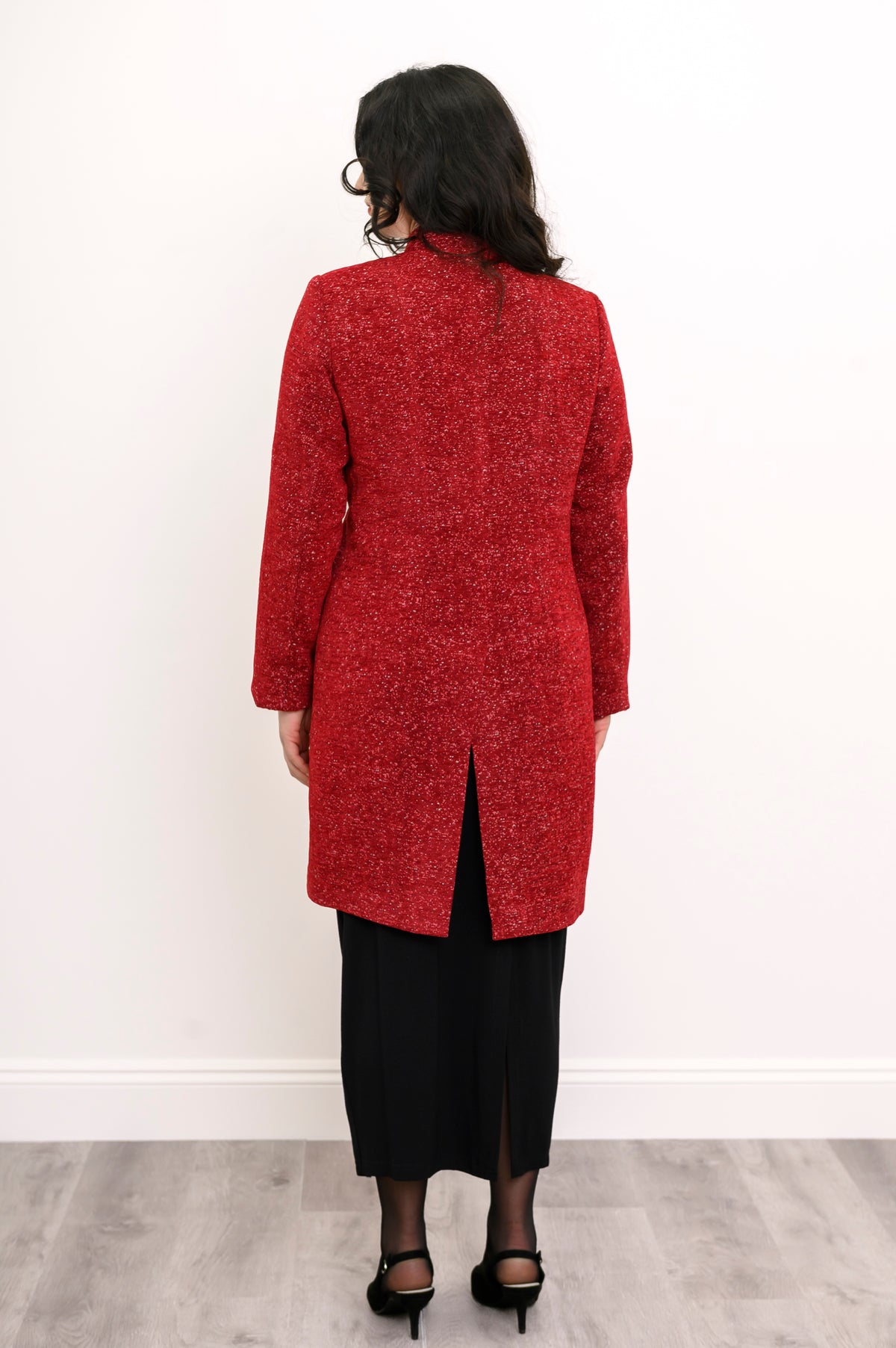 Back view of woman wearing long wool coat in red with white sparkles and split hem
