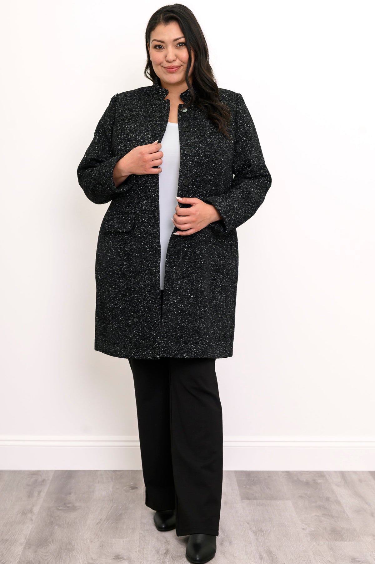 Woman wearing black textured coat with pockets and black pants on a white background, front view