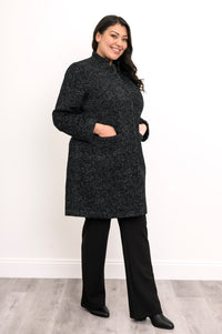 Woman wearing black/dark grey collared coat with hands in pockets and a black pants
