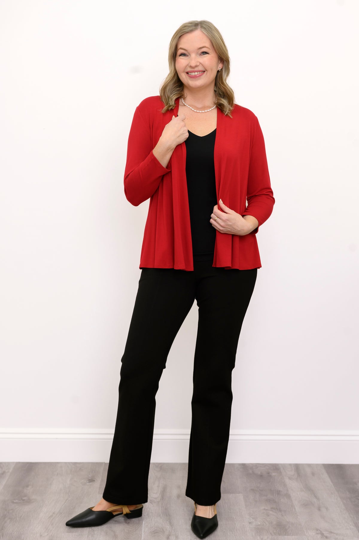Front view of woman wearing a red cardigan, black top, and black pants on a white background
