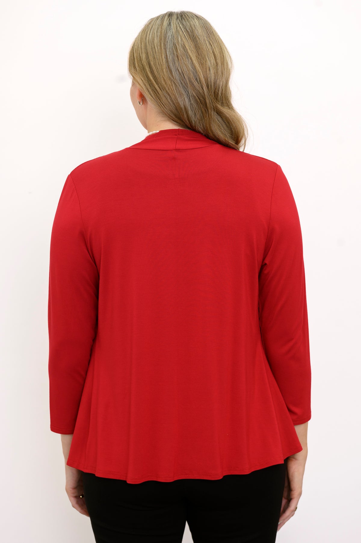 Back view of woman wearing a red cardigan, black top, and black pants on a white background