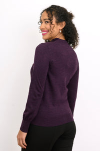 Back view of woman wearing a purple cardigan on a purple top and black pants against a background
