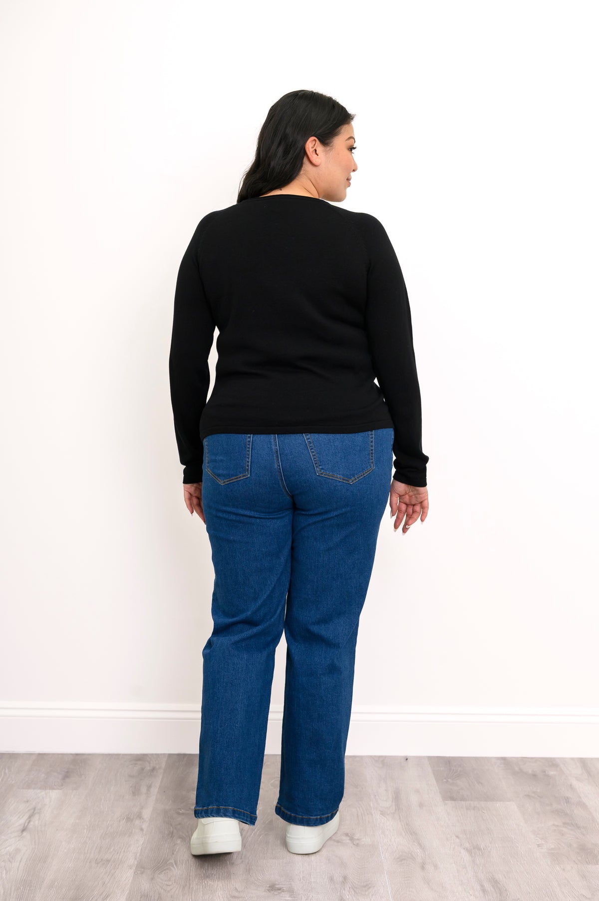 Back view of an onyx raglan sweater, showcasing a seamless rear panel, long sleeves, and classic blue denim jeans.