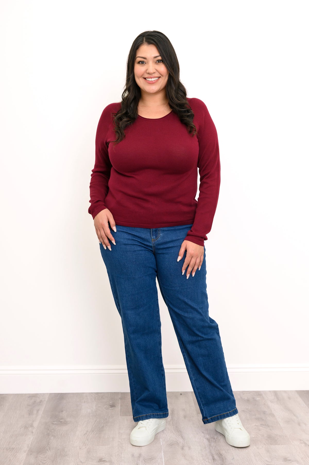 Deep maroon long-sleeve knit shirt featuring a flat finished hemline, styled simply with denim trousers, front view.