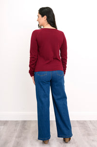 Back view of a women's long-sleeve dark red knit top, styled with blue jeans against a plain white backdrop.