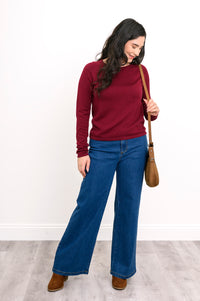 Model wearing a rich wine-red sweater layer and blue denim pants, styled for a comfortable, casual winter look.