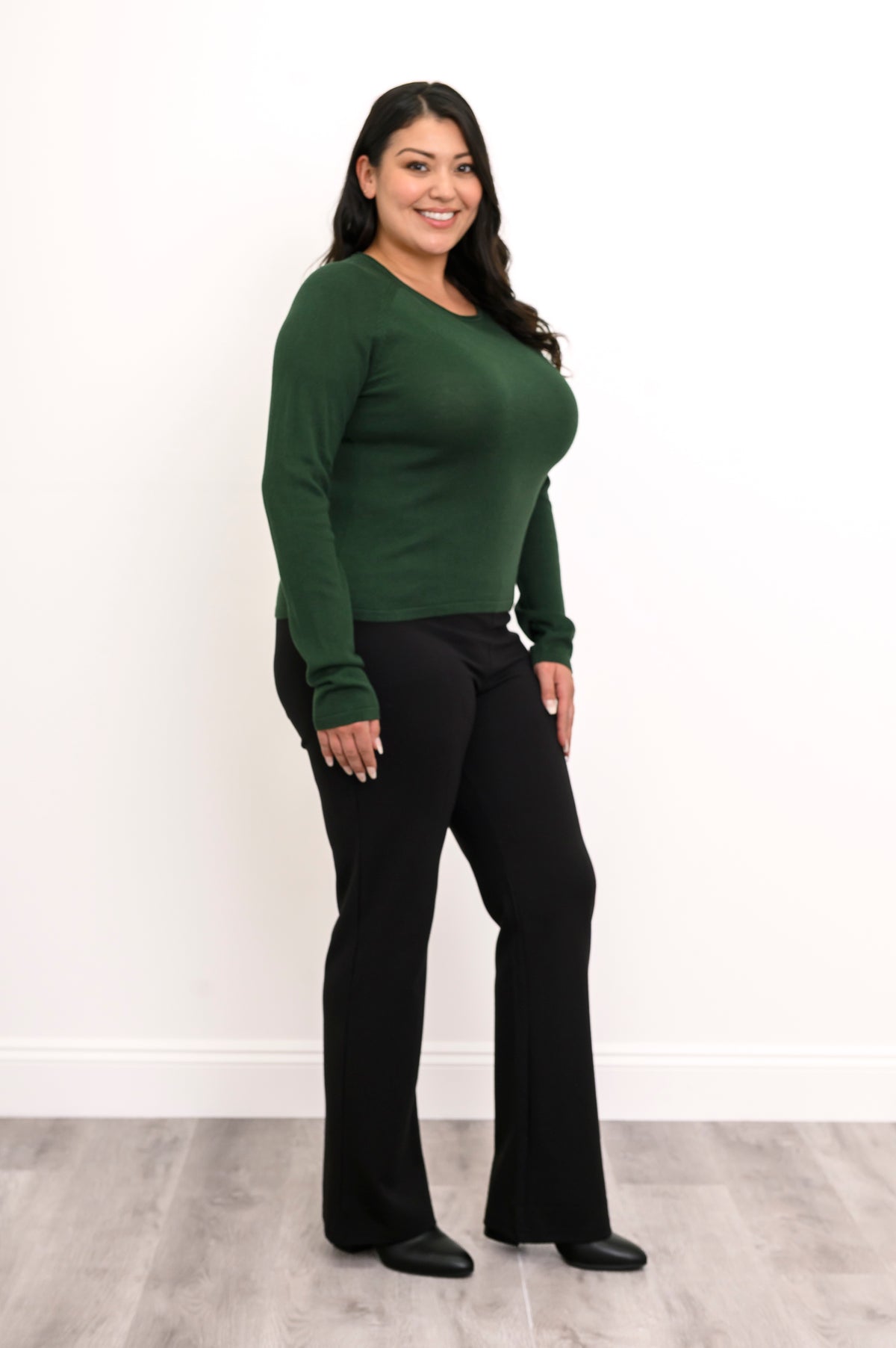 Side view of a women's deep moss knit top, illustrating the smooth side drape and mid-hip length profile.