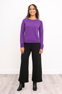 Aubergine knit pullover with long raglan sleeves and a rounded hem, shown on a model standing against a white wall.