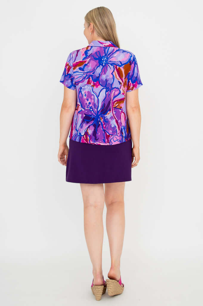 Back view of woman in purple and magenta abstract print short sleeve top and skirt