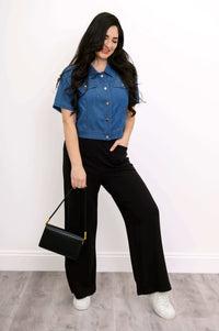 Model styling a cropped denim jacket with black purse and black wide-leg trousers