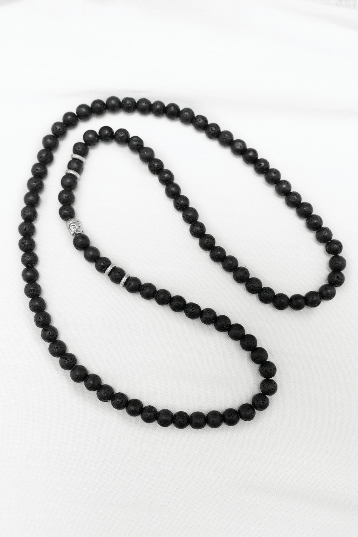 Black lava stone mala necklace with silver accents on white cloth