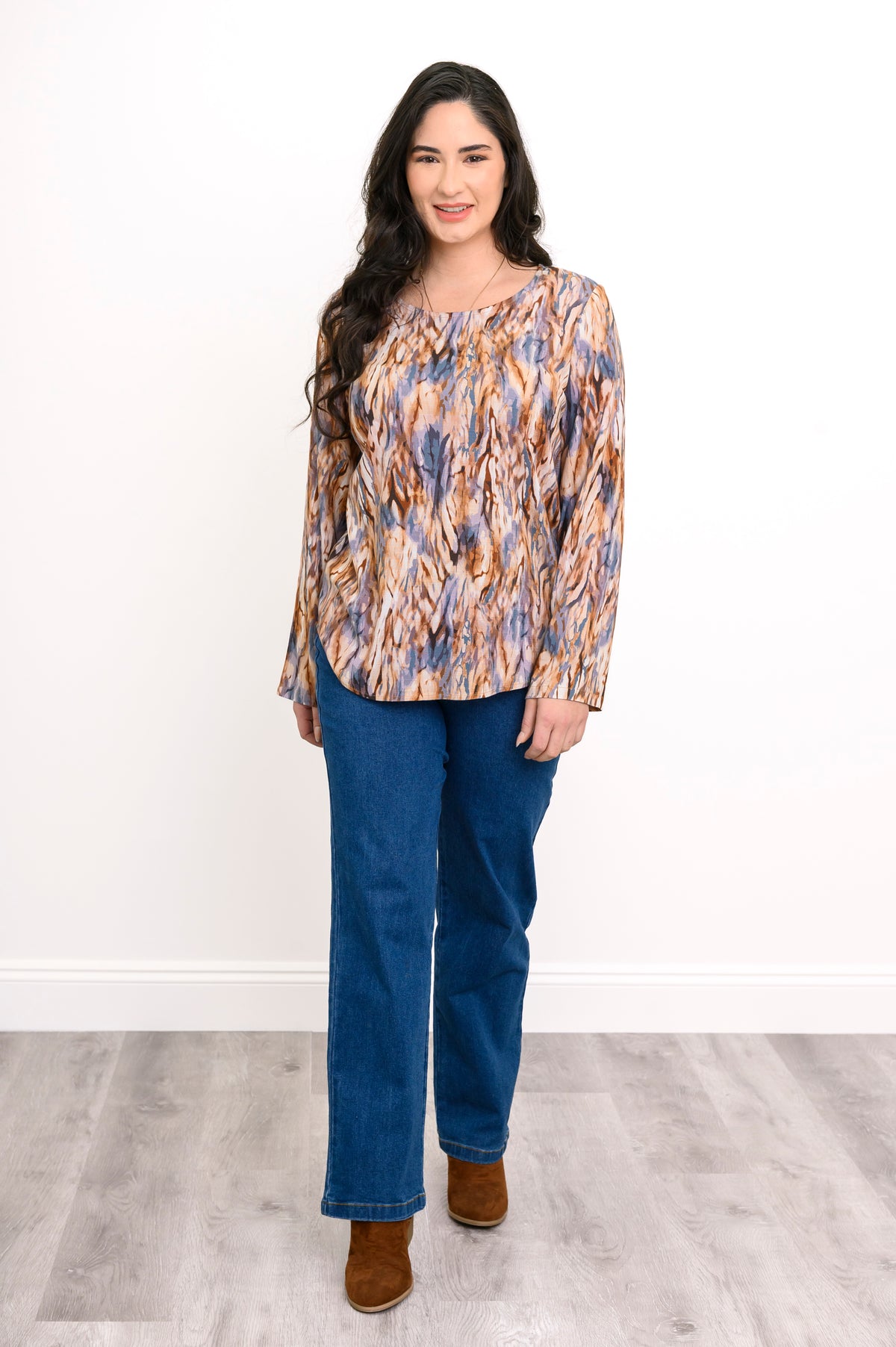 Full-length front view of a woman wearing a long-sleeve patterned blouse in earth tones with blue jeans