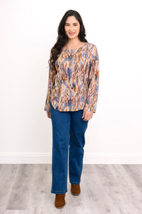 Full-length front view of a woman wearing a long-sleeve patterned blouse in earth tones with blue jeans