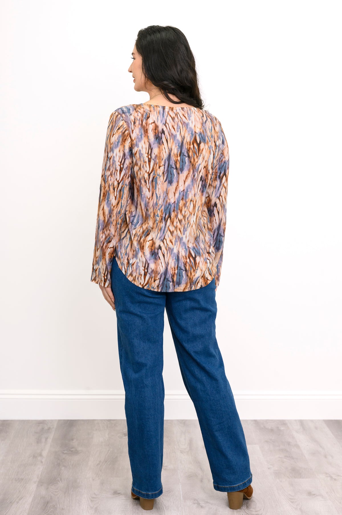 Straight-on full body portrait of a women's abstract print long-sleeve shirt paired with jeans