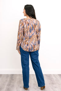 Straight-on full body portrait of a women's abstract print long-sleeve shirt paired with jeans