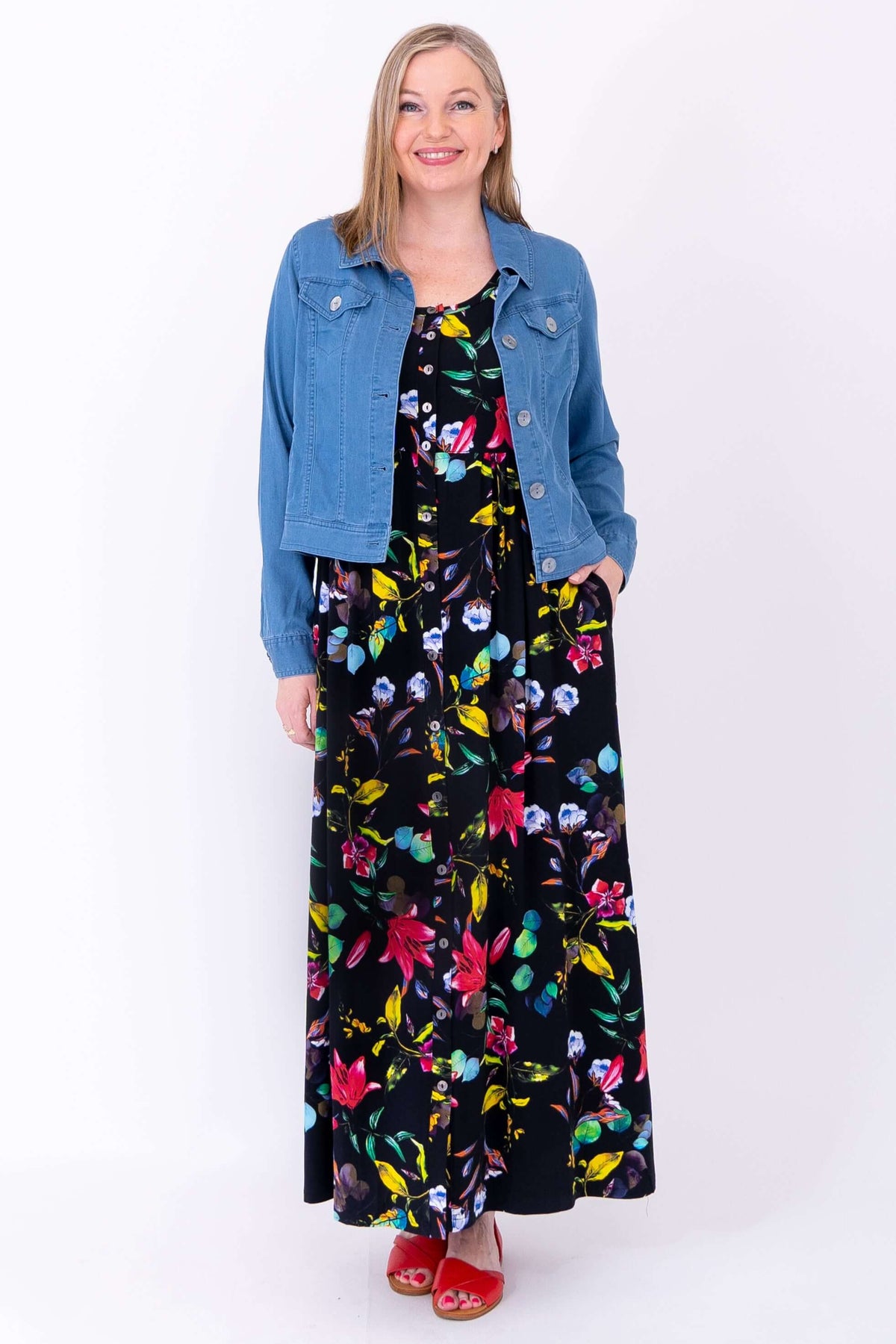 Woman in bamboo maxi dress with colorful florals, styled with a light denim jacket and red sandals