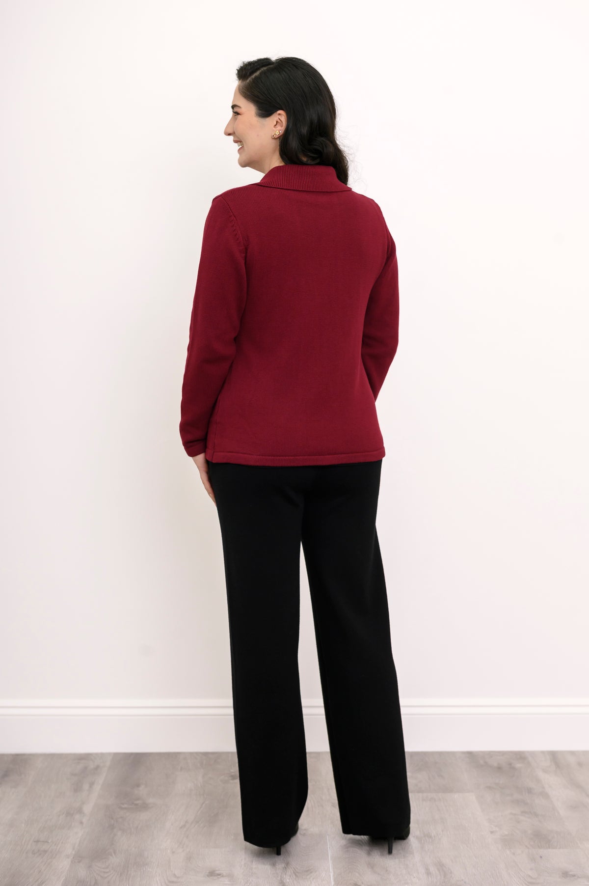 Back view of a woman wearing a fitted hip-length burgundy cotton sweater showcasing the clean tailoring and shoulder fit.