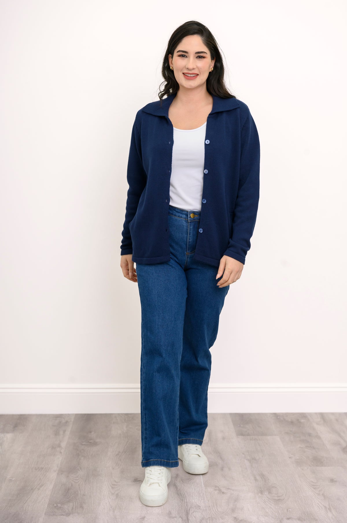 Full length shot of a woman wearing a fitted navy blue cotton cardigan sweater and denim pants against a white background.