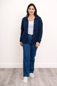 Full length shot of a woman wearing a fitted navy blue cotton cardigan sweater and denim pants against a white background.