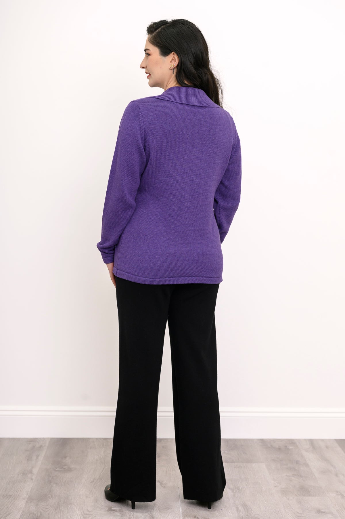 Back view of a violet knit cardigan, showcasing a seamless rear panel, straight waist hem, and black trousers.