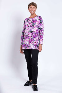 Woman modeling long sleeve floral tunic with black trousers and black shoes