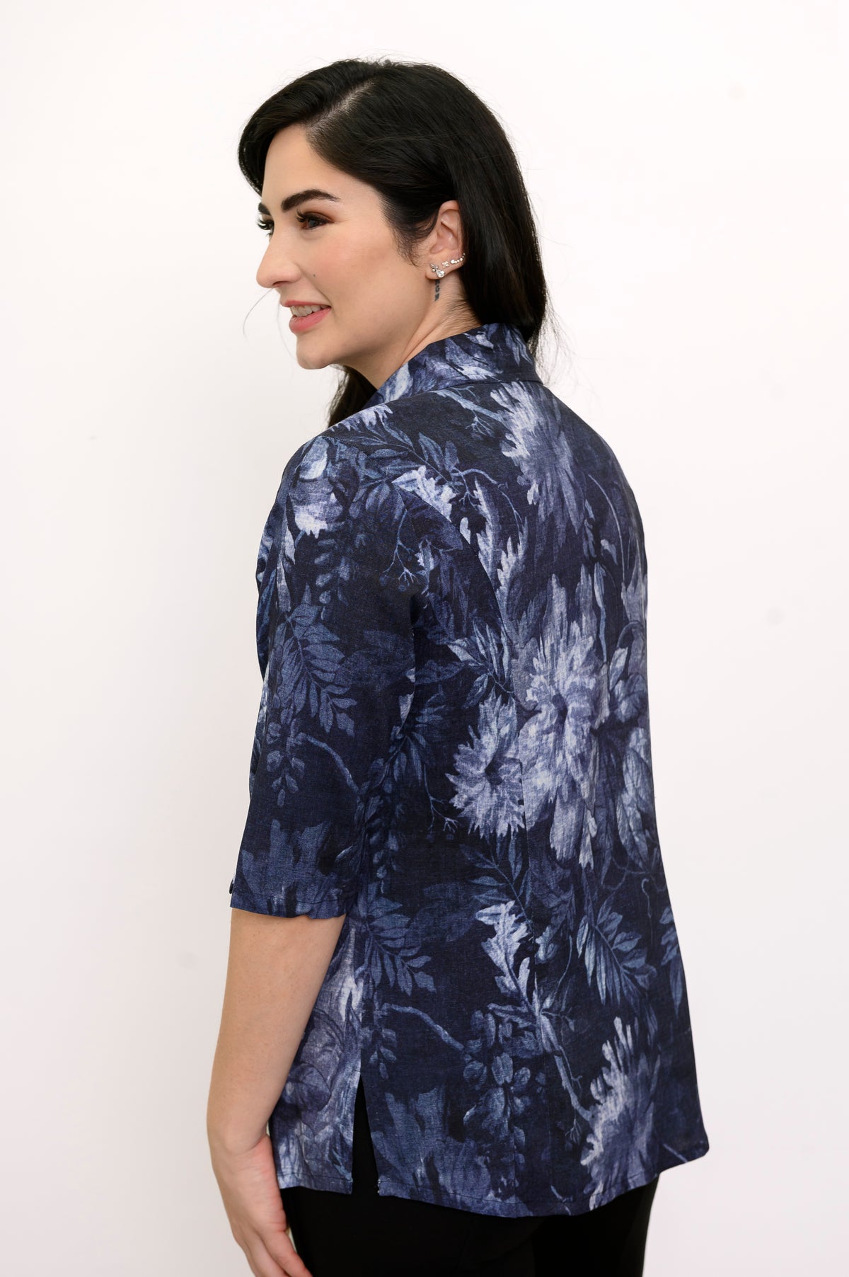 Woman wearing a navy blue floral patterned shirt and black pants against a white background, back view
