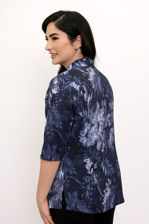 Woman wearing a navy blue floral patterned shirt and black pants against a white background, back view