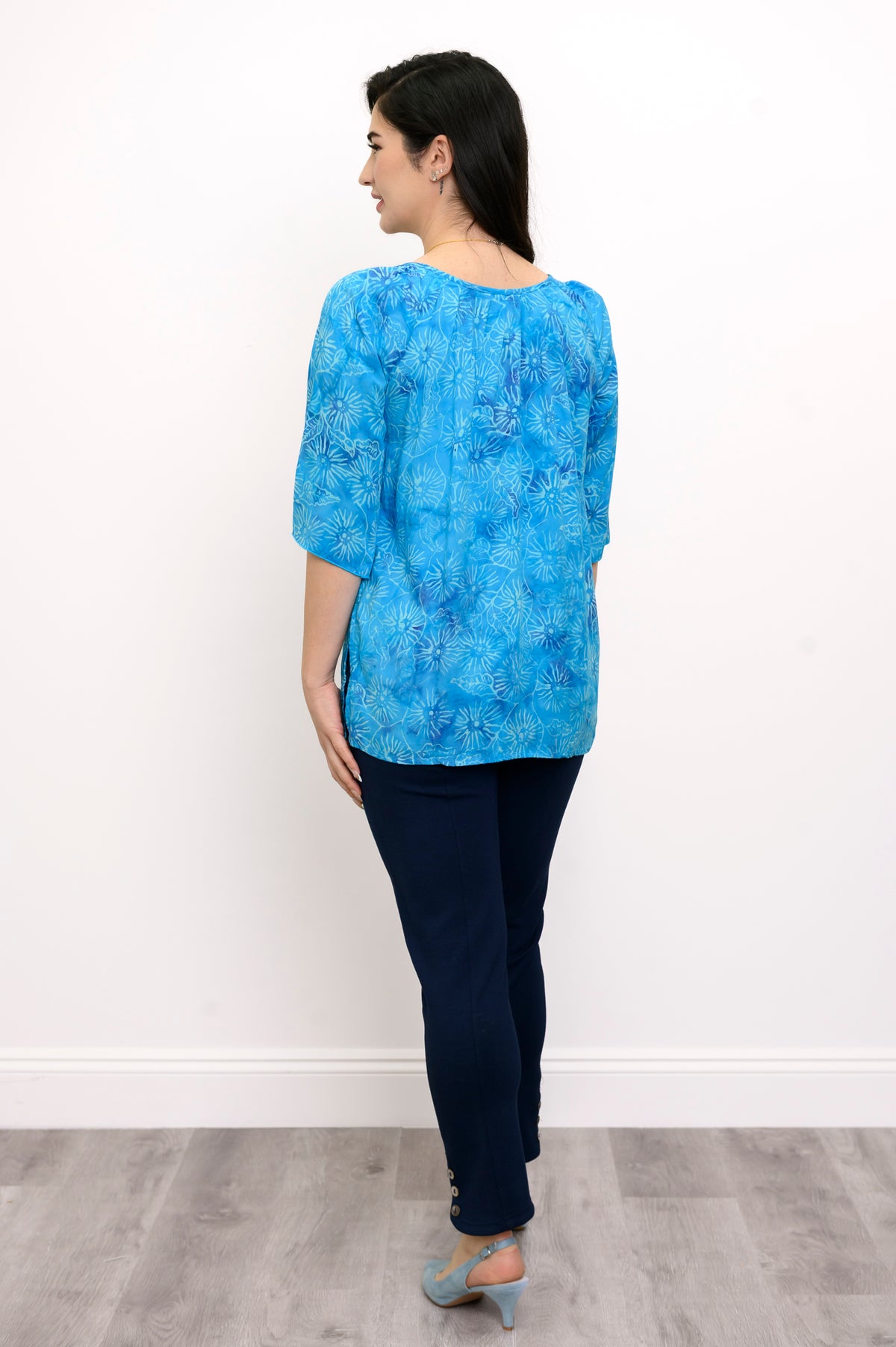 Woman wearing a blue floral top and navy pants on a white background, full body back view