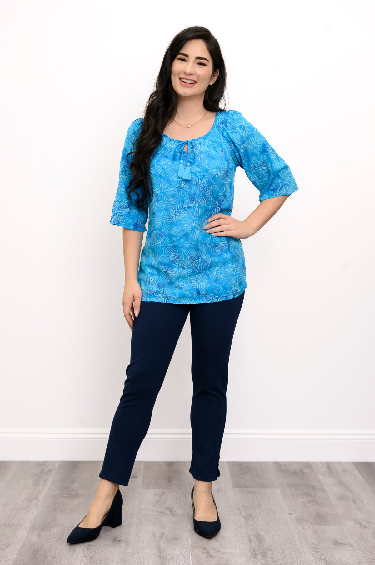 Woman wearing a blue floral top and navy pants on a white background, full body front view