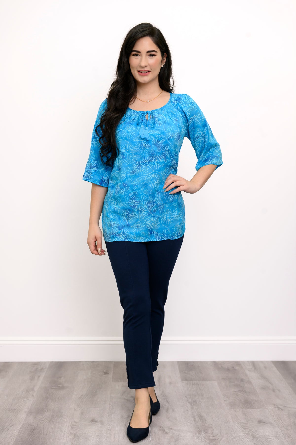 Woman wearing a blue floral top and navy pants on a white background, full body front view