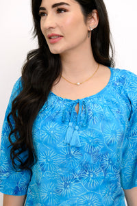 Woman wearing a blue floral top and gold pearl necklace on a white background, close up view
